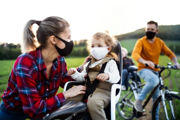 Family with two small children on cycling trip in nature, wearing face masks.